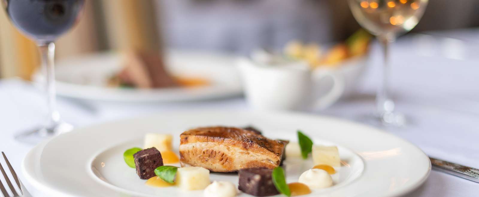 Pork dish on a table with white and red wine