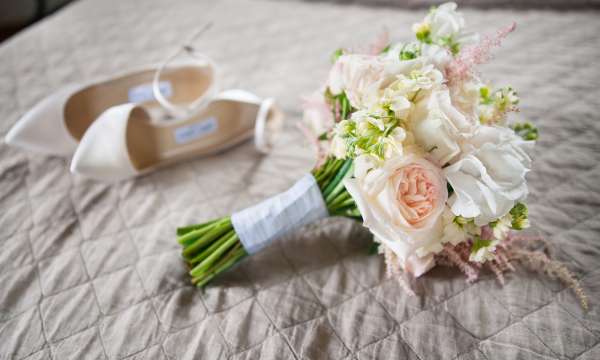 Brides bouquet and shoes placed on top of a bed
