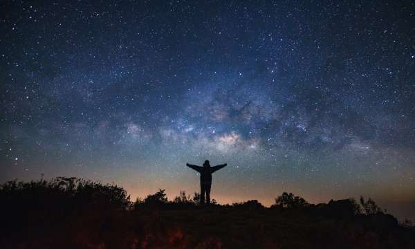 Silhouette standing on a hill looking up at the sky 